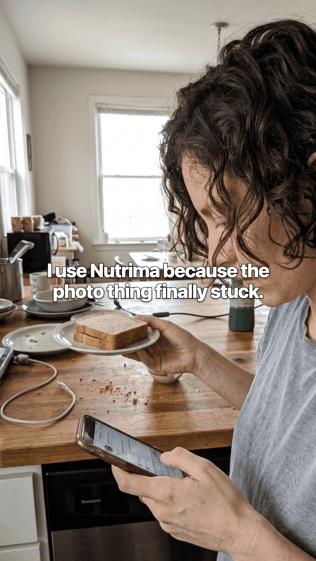 A woman in a kitchen looking at her phone, a plate of toast in her other hand, with a line of the post across the photo.
