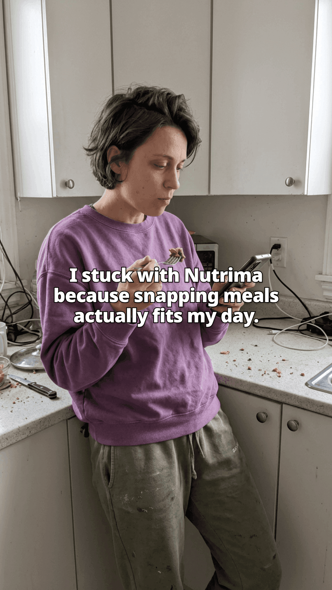 A woman leaning against a kitchen counter with a forkful of food in one hand and her phone in the other, with a line of the post across the photo.